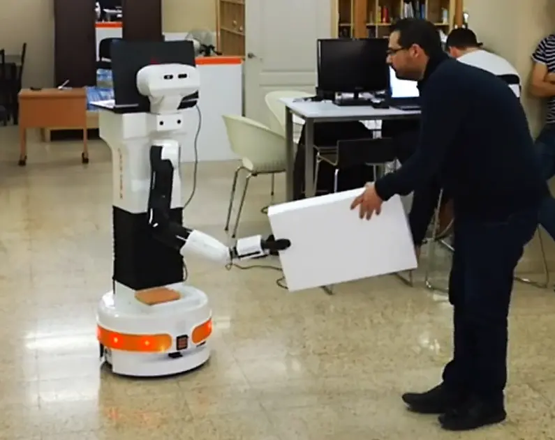 The mobile manipulator TIAGo robot helps a man with a box during the Project Co4Robots